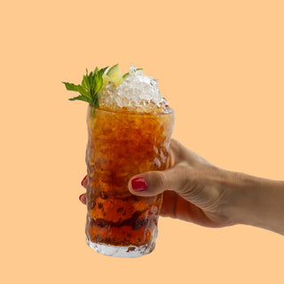 Hand holding a glass of refreshing iced tea made from Herbaly's Wellness Iced Tea Pitcher Size showing the drink's clarity and ice cubes